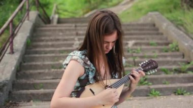 Genç ve güzel bir kız merdivenlerde otururken müzik aleti mandolini çalıyor.