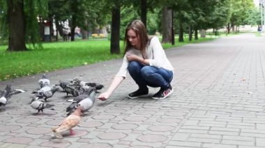 Çekici, mutlu kız parkta güvercinleri elle besliyor. Avuçlarının içinde yulaf tutuyor. Güvercinler ellerinden gagalar. 