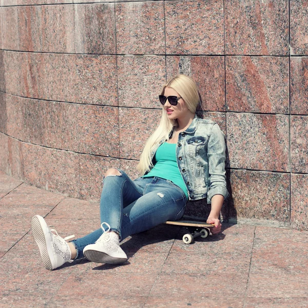Девушка в куртке сидит на скейтборде — стоковое фото