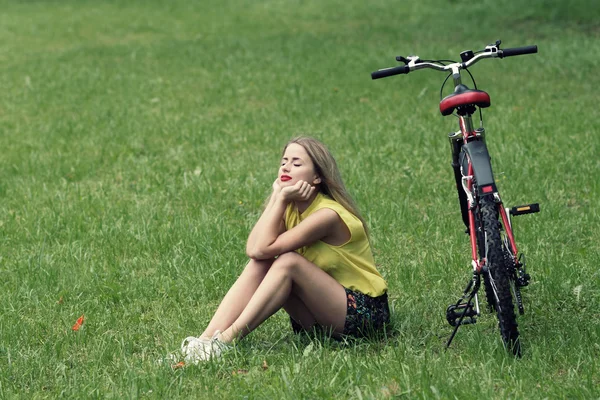 Ung flicka och cykel på grön gräsmatta — Stockfoto