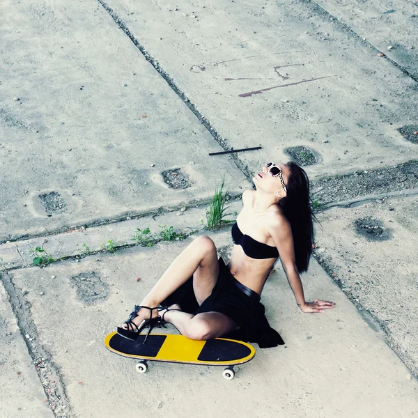 Donna in occhiali da sole seduta su uno skateboard — Foto Stock