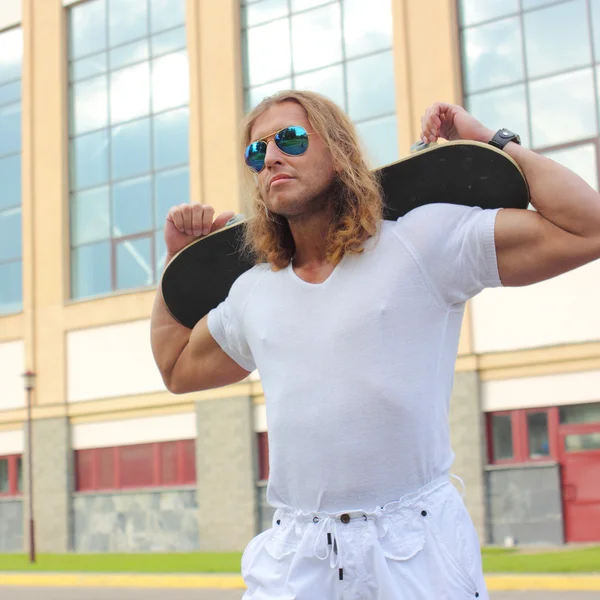 Musclé homme aux cheveux longs avec planche à roulettes — Photo