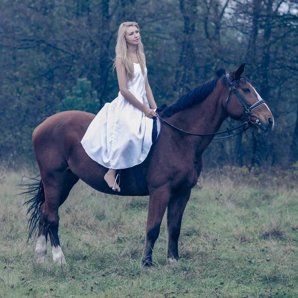 Girl in white dress on a horse in the forest