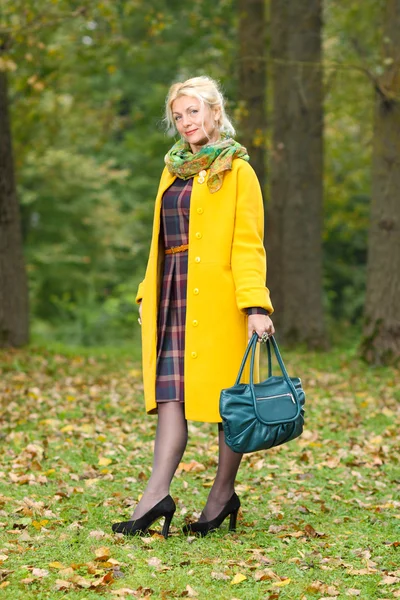 Senior vrouw met een gele vacht wandelingen in het park — Stockfoto