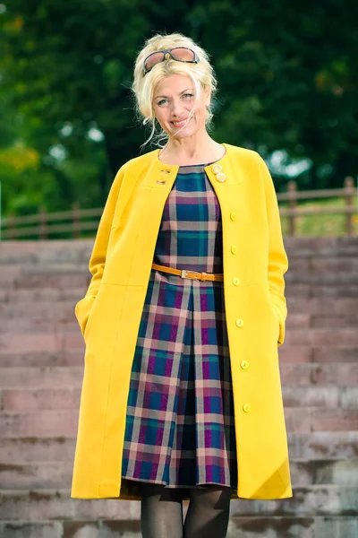 Donna anziana con un cappotto giallo cammina nel parco — Foto Stock