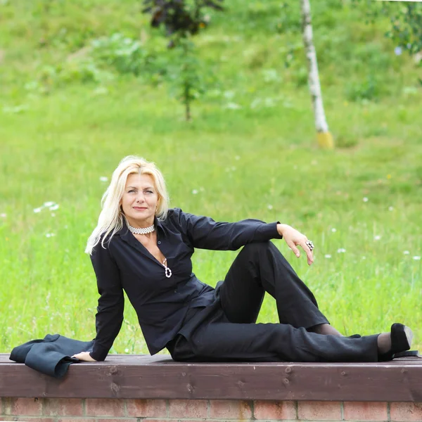 Vrouw in zwart pak zittend op het gras — Stockfoto