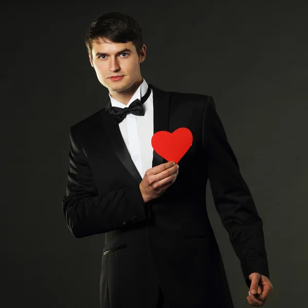 Man in a tuxedo with a red paper heart — Stock Photo, Image