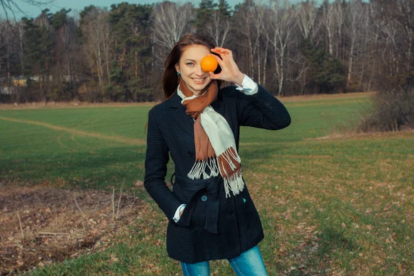 Flicka med en orange frukt utomhus — Stockfoto