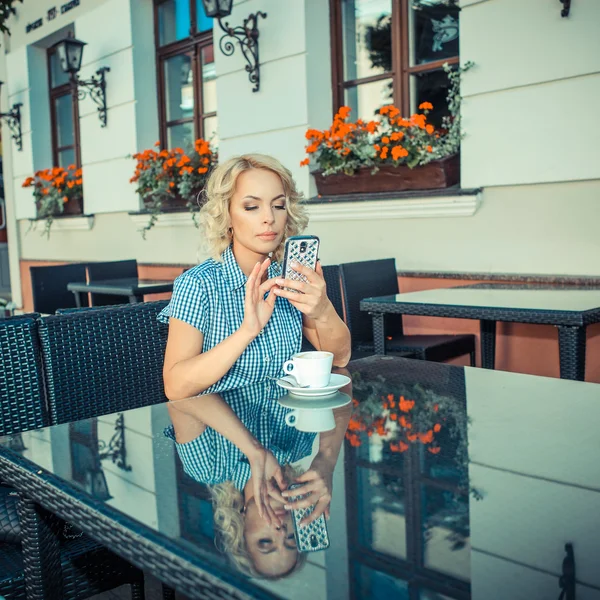 Blond girl with phone in an outdoor cafe — Stockfoto