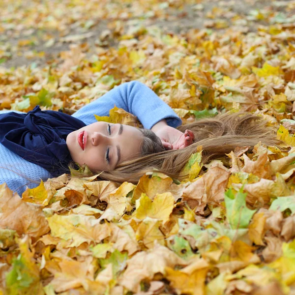 Menina deitada entre folhas amarelas — Fotografia de Stock