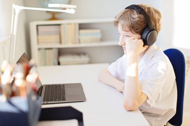 pozitif gülümseyen çocuk evde bilgisayar ve kulaklık kullanarak koronavirüs salgını sırasında öğreniyor.