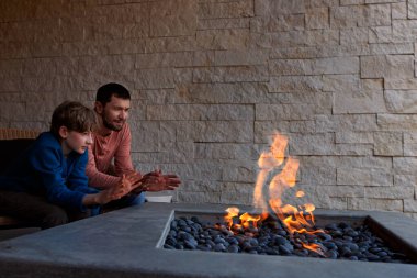 view of firepit and happy smiling family of two, father and son, warming their hands by the fire and enjoying time together  clipart