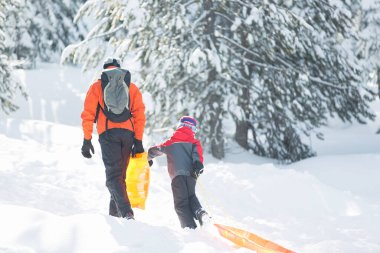 Heyecanlı küçük çocuk ve babası kızakla kaymaya hazır, birlikte kış eğlencelerinin tadını çıkarıyorlar.
