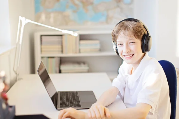 ラップトップとヘッドフォンを使用してコロナウイルスのパンデミックの間に自宅で肯定的な笑顔の少年オンライン学習 ストック画像