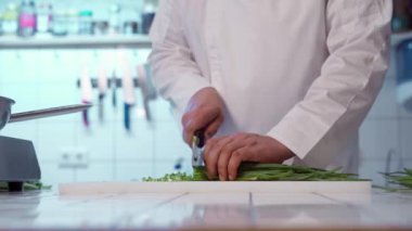Şef kesme tahtasındaki keskin bıçakla taze soğan kesiyor..