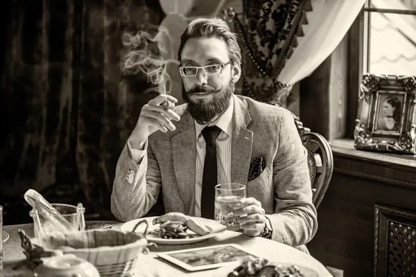 Homem com barba e bigode, fumando um charuto durante o jantar — Fotografia de Stock