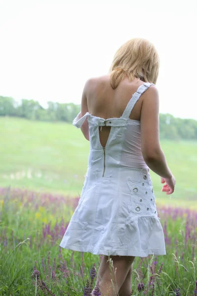 Girl in white dress going away on meadow — Stock Photo, Image