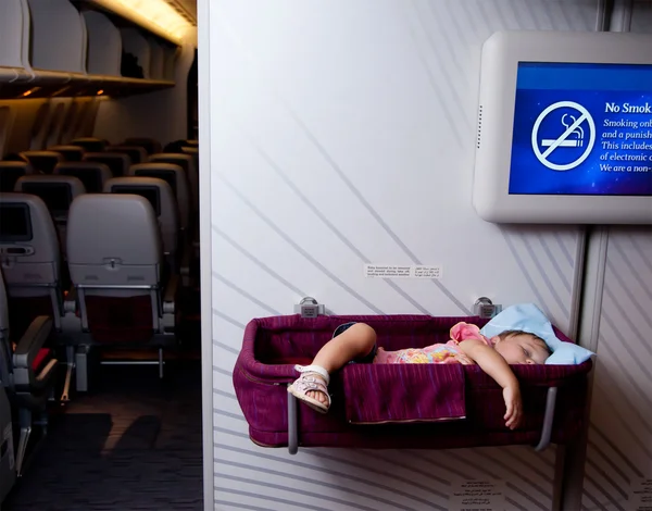 छोटे दो साल की बेबी गर्ल एक विमान पर एक बेसिनेट में सोती है — स्टॉक फ़ोटो, इमेज