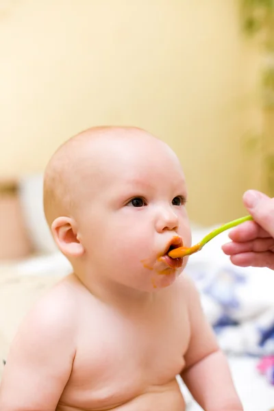 Mãe alimenta o bebê por purê de melão e cenoura com colher de plástico — Fotografia de Stock