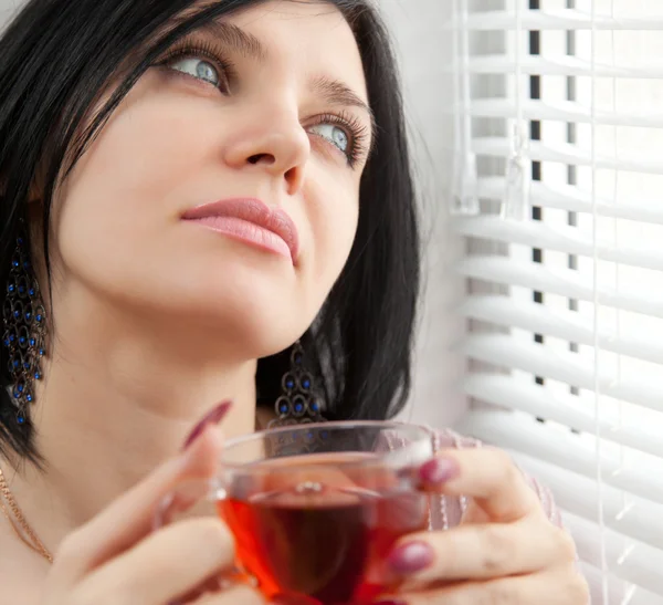 Thoughtful brunette girl drinking tea at the window — Stock Photo, Image