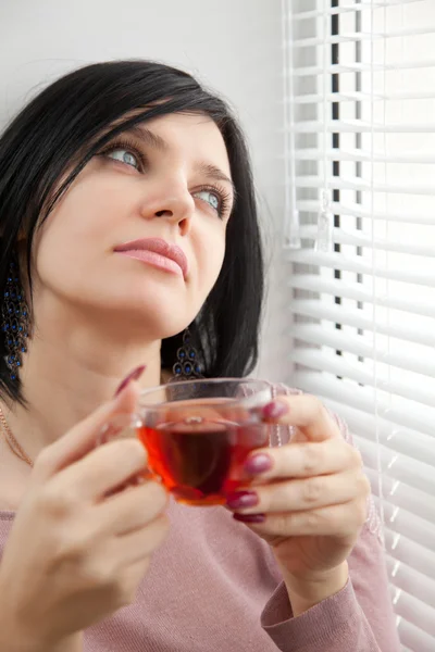 Thoughtful brunette girl drinking tea at the window — Stock Photo, Image