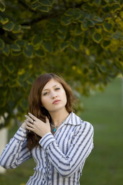 Beauty brunette in a park correct you hairstyle — Stock Photo, Image