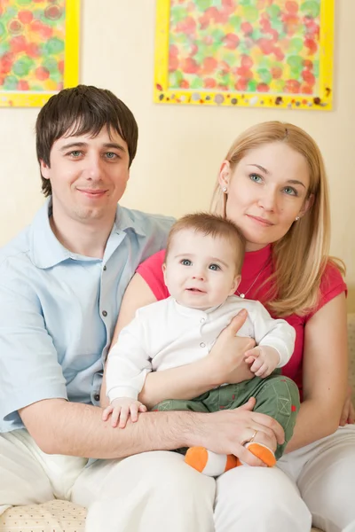 Young happy family sitting on sofa at home — Stock Photo, Image