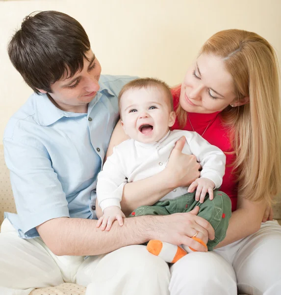 Young happy family sitting on sofa at home — Stock Photo, Image