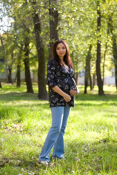 Pregnant woman in blue jeans saunter in park — Stock Photo, Image