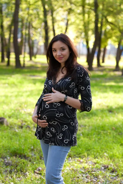 Pregnant woman in blue jeans walking in park — Stock Photo, Image