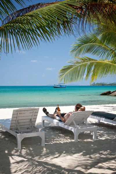 Человек отдыхает с пивом в тени под пальмами на пляже — стоковое фото
