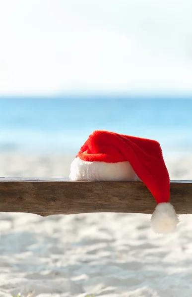 Red Santa's hat on wooden bench at the tropical beach — Stock Photo, Image