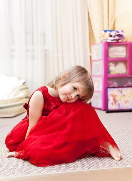 Kleines Mädchen in einem schönen roten Kleid sitzt in ihrem Schlafzimmer — Stockfoto