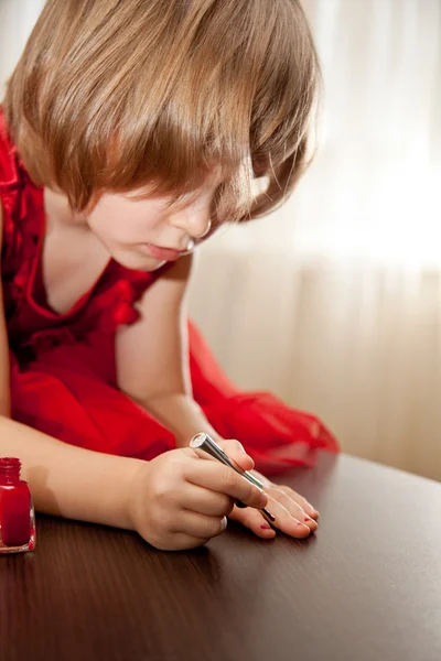 Маленькая девочка в красном платье раскрасила ногти лаком для ногтей — стоковое фото