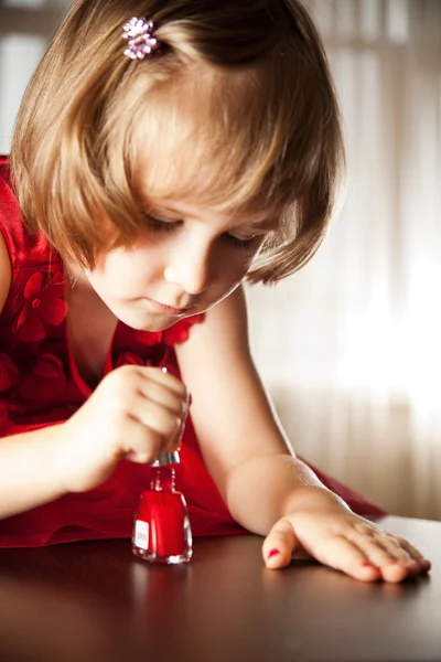 Petite fille dans une robe rouge peinte ongles avec vernis à ongles — Photo