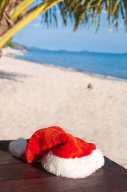Plaj sandalyesini palmiye ağacının altında asılı kırmızı Noel Baba'nın şapka