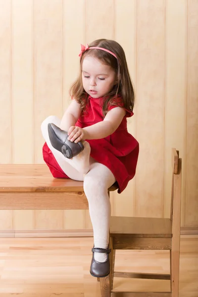 Маленькая девочка сидит на столе и надевает ботинки — стоковое фото