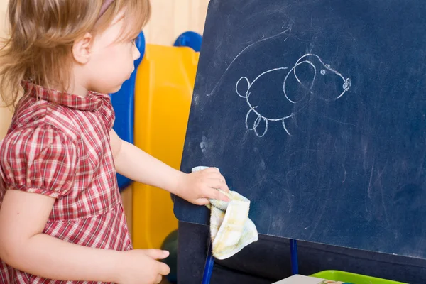Kleines Mädchen wischt Zeichnung auf Schiefertafel — Stockfoto