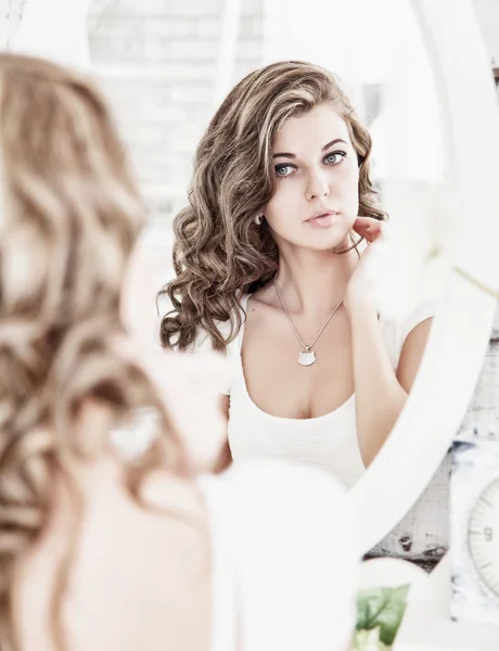 Молодая красивая женщина смотрит на свое лицо в зеркало — стоковое фото