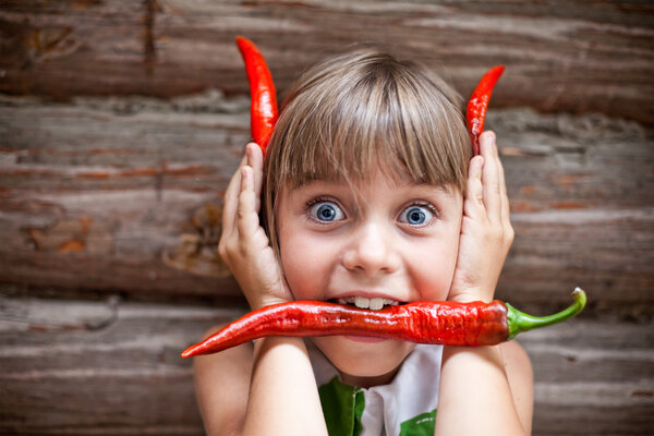 Девушка с красным острым перцем чили во рту показывает дьявольские рога
