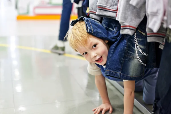 Niño jugando a las escondidas bajo el estante de ropa en la tienda — Foto de Stock