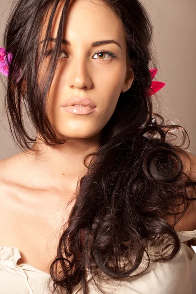 Portrait of young brunette woman with flower in curly hair — Stock Photo, Image