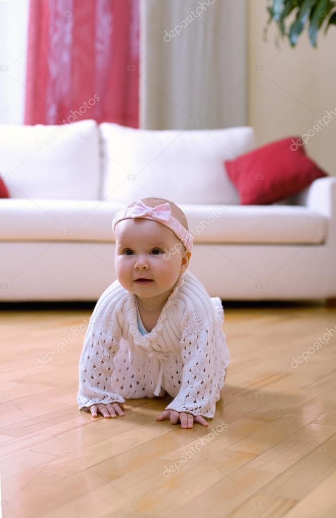 Happy eight month old baby girl crawling on a hardwood floor