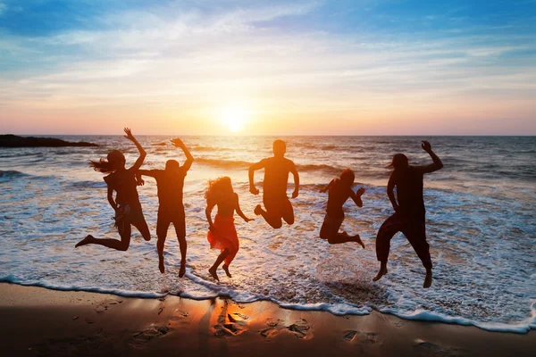 Six people jumping on beach at sunset.