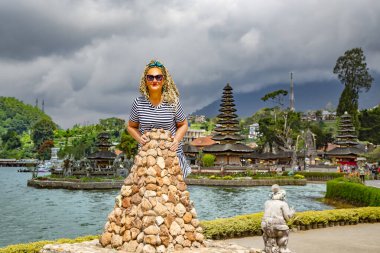 UBUD, BALI, INDONESIA, AUGust, 2019: Pura Ulun Danu Batur 'da kıvırcık saçlı güzel bir kadın, Endonezya' nın Bali kentinde, Beratan Gölü üzerinde yer alan ve sönmüş bir volkanın kraterinde yer alan bir tapınaktır.
