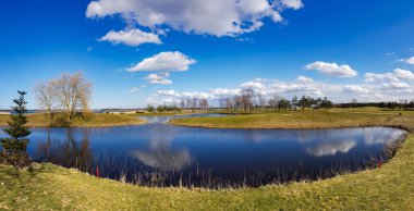 Riga, Letonya 'daki Kisezers kıyılarındaki su basmış çayırlar üzerindeki küçük göllerle güneşli bahar manzarası. Suya beyaz kümülüs bulutları yansıyor..