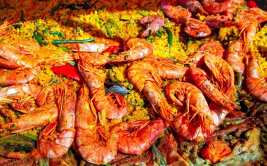 Sokağın ortasında tavada pişmiş yeşil fasulyeli İspanyol paella, büyük karides ve diğer deniz ürünleri..