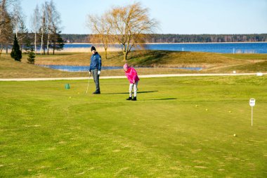 LATVIA, RIGA, APRIL, 2021 - Aile Riga, Letonya 'daki güzel Kisezers gölünün kıyısında golf oynuyor. İnsanların yaşam tarzı yeşil çimlerin üzerinde golf oynuyor..
