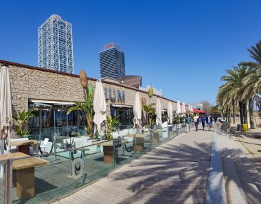 İspanya, BARCELONA, MARCH, 2021: Port Olimpic yakınlarındaki barlar ve restoranlarla birlikte arka planda Mapfre kulesi Vila Olimpica, Barcelona, Katalonya, İspanya.