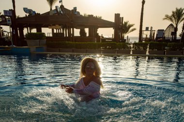 Kıvırcık saçlı neşeli kız gün doğumunda Sharm el Sheikh, Mısır 'da havuza su sıçratıyor. Otelde ve denizde rahatlama kavramı.